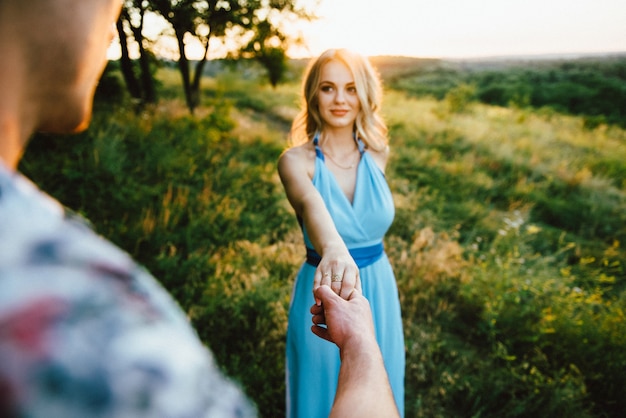 Mujer rubia con cabello suelto con un vestido azul claro y un chico a la luz del atardecer en la naturaleza