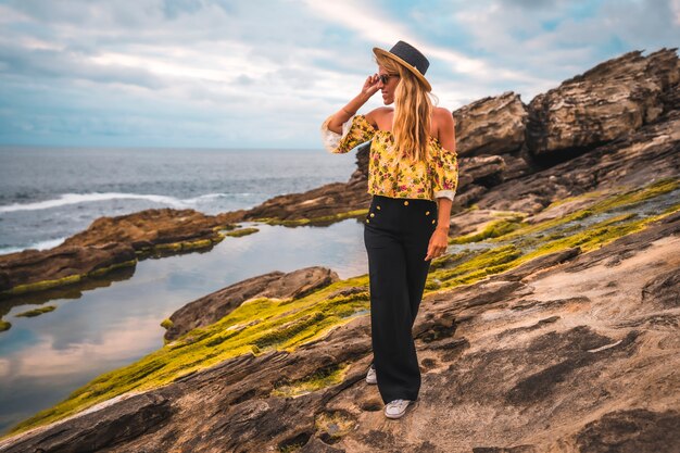 Mujer rubia en una camisa floral en la playa rocosa