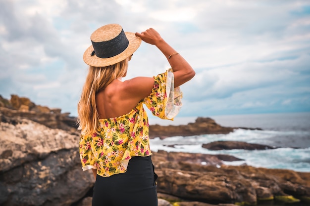 Mujer rubia en una camisa floral en la playa rocosa