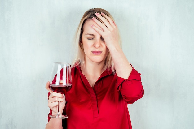 Una mujer rubia con una camisa roja sostiene una copa de vino en sus manos. La idea del alcoholismo, la ruptura de relaciones.