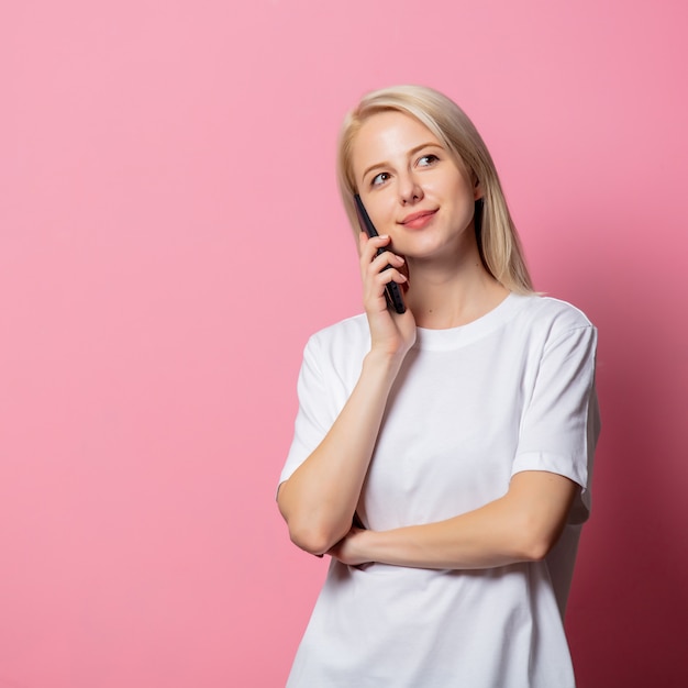 Mujer rubia en camiseta blanca con teléfono móvil en rosa