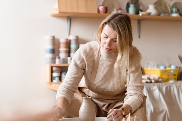 Mujer rubia cansada wirking con torno de alfarería en el taller