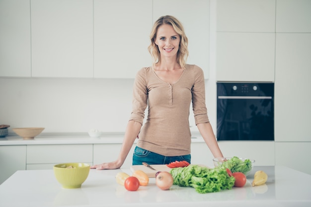 Mujer rubia en casa en la cocina con verduras