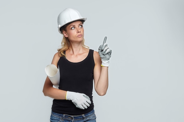 Mujer rubia en casco de construcción apunta al campo en blanco para la colocación del texto