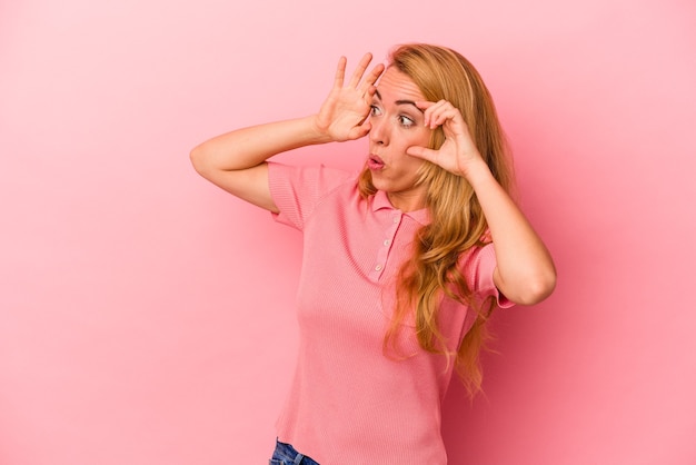 Mujer rubia caucásica aislada sobre fondo rosa manteniendo los ojos abiertos para encontrar una oportunidad de éxito.