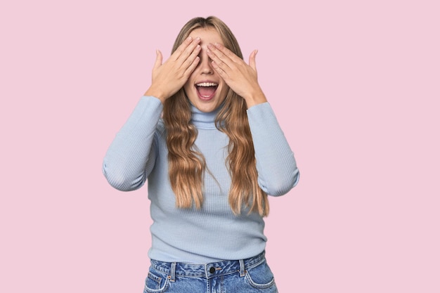 Foto mujer rubia caucásica cubre los ojos con las manos sonríe ampliamente esperando una sorpresa