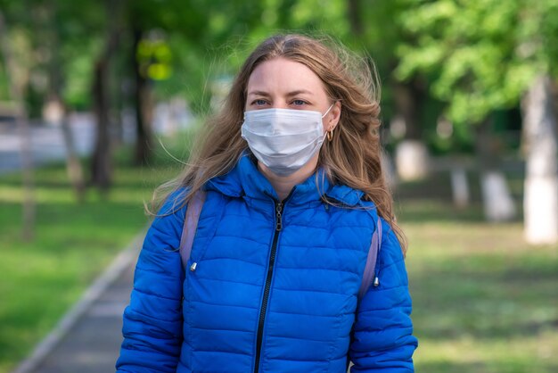 Mujer rubia caucásica en máscara protectora y guantes está caminando por la calle vacía. comportamiento seguro durante una pandemia