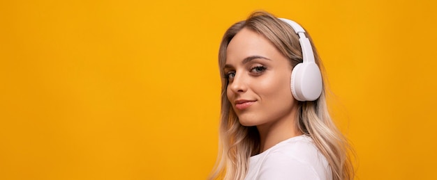 Mujer rubia caucásica posando en auriculares blancos sobre fondo naranja con espacio vacío