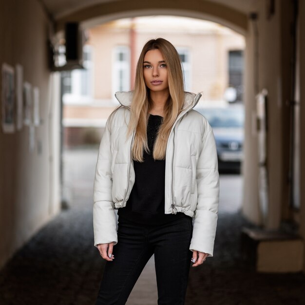 Mujer rubia con una chaqueta blanca en traje negro está posando en la ciudad