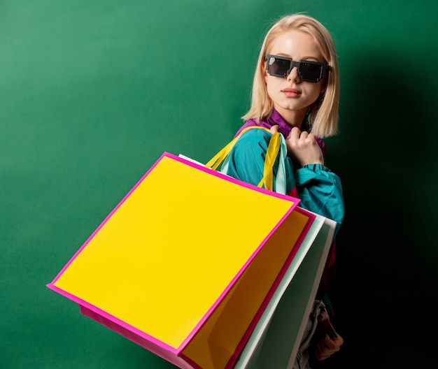 Mujer rubia en chaqueta estilo años 90 con bolsas de compras