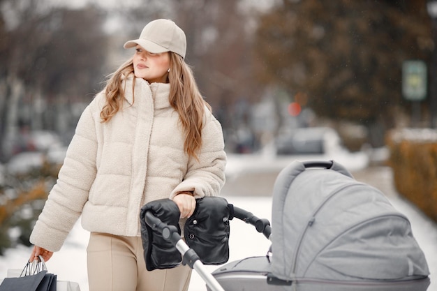 Mujer rubia con cochecitos de bebé caminando por la ciudad con paquetes de compras