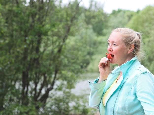 Mujer rubia come fresas en el bosque