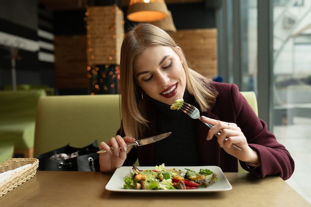 Mujer rubia comiendo ensalada ecológica sabrosa saludable verde en el café de la ciudad