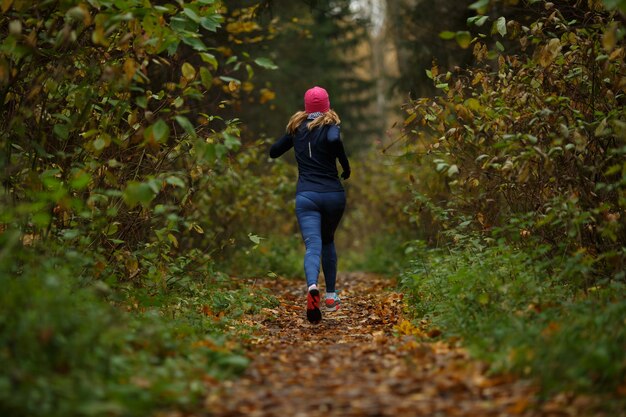 Mujer rubia corriendo en sendero en el parque otoño