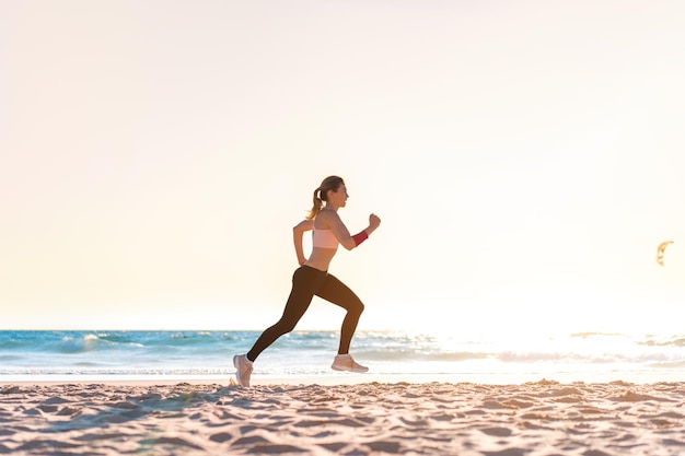 Mujer rubia deportiva corriendo en la playa del océano Joven mujer caucásica haciendo ejercicio al aire libre corriendo a la orilla del mar Concepto de correr saludable y hacer ejercicio al aire libre