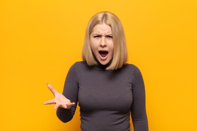 Mujer rubia con enojo, molesto y frustrado gritando wtf