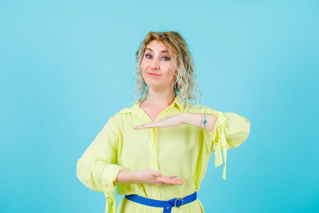 Mujer rubia está mirando a la cámara mostrando un gesto de tamaño sobre fondo azul.