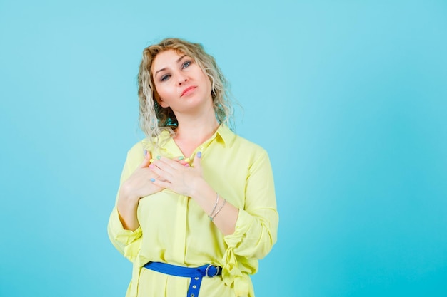 Mujer rubia está mirando a la cámara tomándose de la mano en el hombro sobre fondo azul.