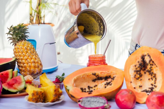 Mujer rubia de estilo de vida mezclando frascos de vidrio de jugo de licuadora con batidos y paja en el balcón de veranofrutas exóticas tropicales en la mesalimpiando el cuerpo de ideas de toxinastemporada de verano