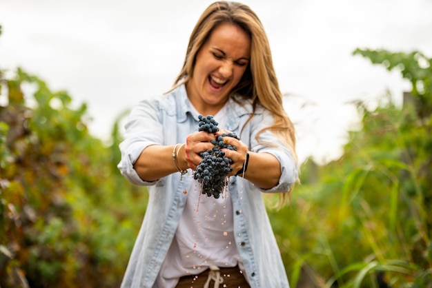 Mujer rubia exprimiendo un racimo de uvas con sus manos