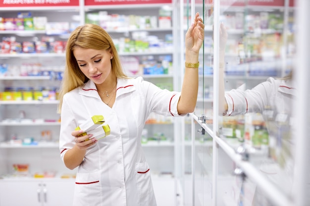 Mujer rubia farmacéutica en uniforme comprobando el stock de surtido en farmacia