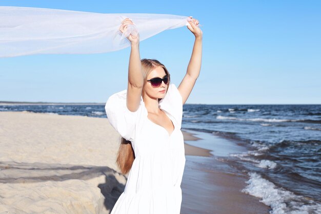 La mujer rubia feliz está atrapando nubes y viento con los brazos en la playa del océano.