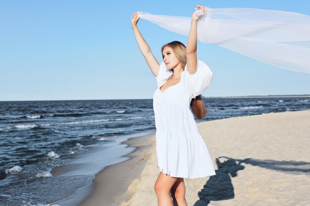 Una mujer rubia feliz está atrapando nubes y viento con sus brazos en la playa del océano