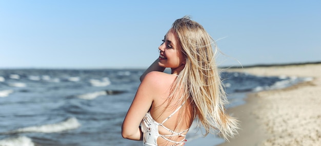 Mujer rubia feliz en la felicidad de la felicidad libre en la playa del océano de pie derecho y posando