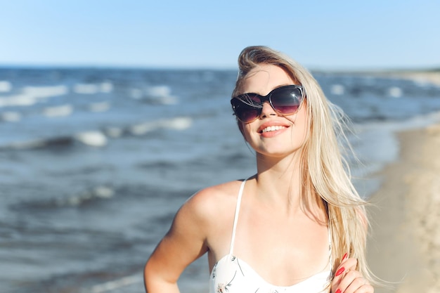 Mujer rubia feliz en la felicidad libre en la playa del océano de pie con gafas de sol y posando.