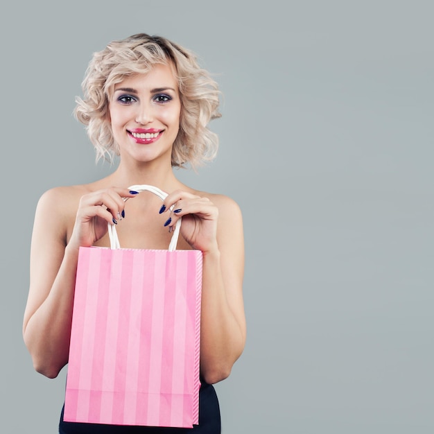 Mujer rubia feliz sosteniendo bolsas de compras rosas y sonriendo