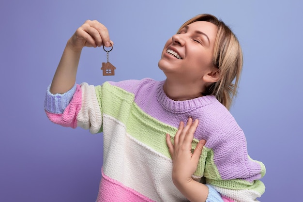 Mujer rubia feliz sosteniendo llavero de nuevo apartamento sobre fondo púrpura