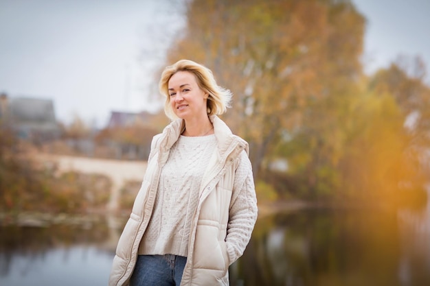 Mujer rubia feliz en suéter blanco está mirando a la cámara y sonriendo