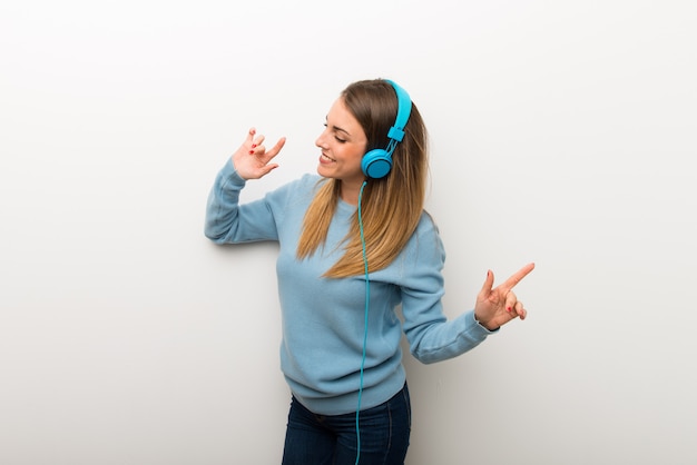 Mujer rubia en el fondo blanco aislado que escucha la música con los auriculares y el baile