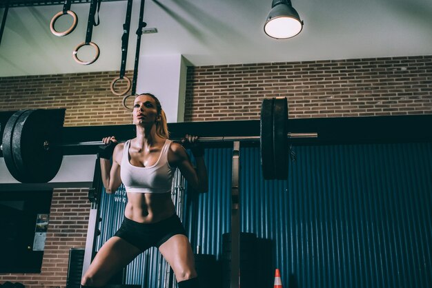 Mujer rubia en forma entrenando levantando una barra de pesas en el gimnasio