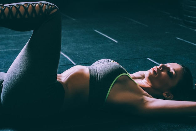 Una mujer rubia en forma tirada en el suelo estirándose y haciendo abdominales en el gimnasio