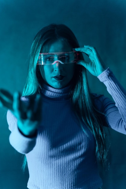 Mujer rubia con gafas futuristas gesticulando contra un fondo azul.