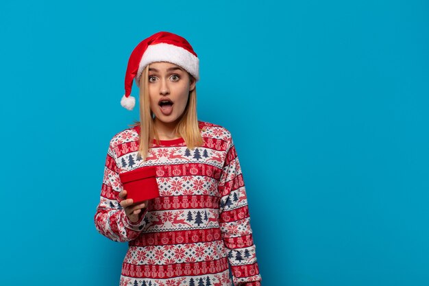 Mujer rubia con gorro de Papá Noel que parece muy conmocionada o sorprendida, mirando con la boca abierta diciendo wow