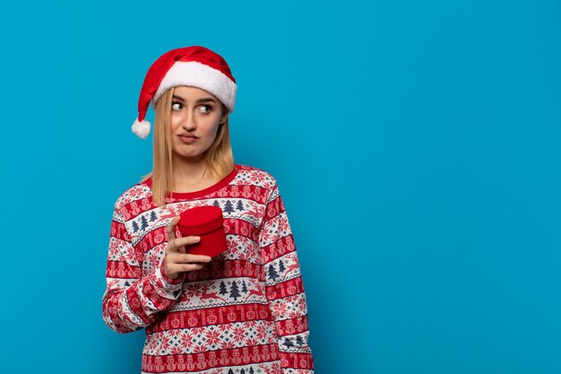 Mujer rubia con gorro de Papá Noel que se siente triste, molesta o enojada y mirando hacia un lado con una actitud negativa, frunciendo el ceño en desacuerdo