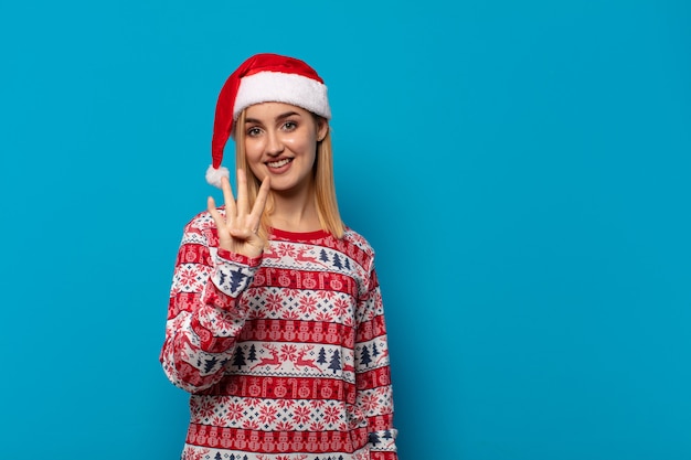 Mujer rubia con gorro de Papá Noel sonriendo y mirando amistosamente, mostrando el número cuatro o cuarto con la mano hacia adelante, contando hacia atrás