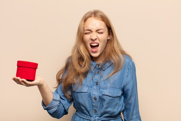 Mujer rubia gritando agresivamente, luciendo muy enojada, frustrada, indignada o molesta, gritando no