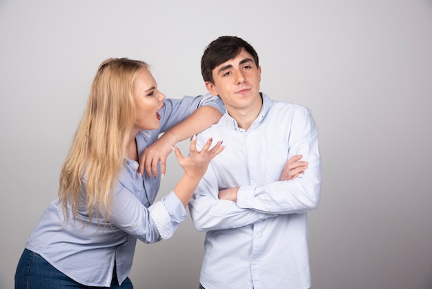 Mujer rubia gritando al modelo de chico morena contra la pared gris.