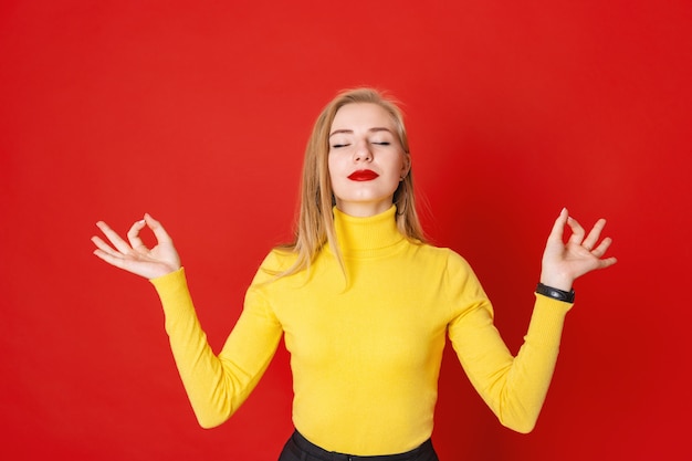 Mujer rubia hermosa que medita con los ojos cerrados en fondo rojo.