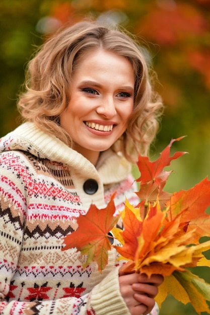 Mujer rubia con hojas de otoño posando al aire libre