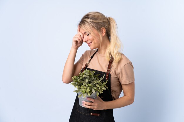 Mujer rubia jardinero sosteniendo una planta sobre risa aislada