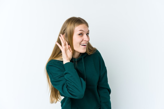 Mujer rubia joven aislada en la pared blanca tratando de escuchar un chisme.