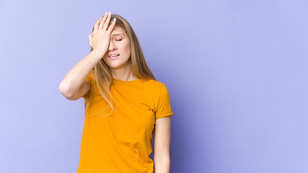 Mujer rubia joven aislada en la pared púrpura cansada y con mucho sueño manteniendo la mano en la cabeza.