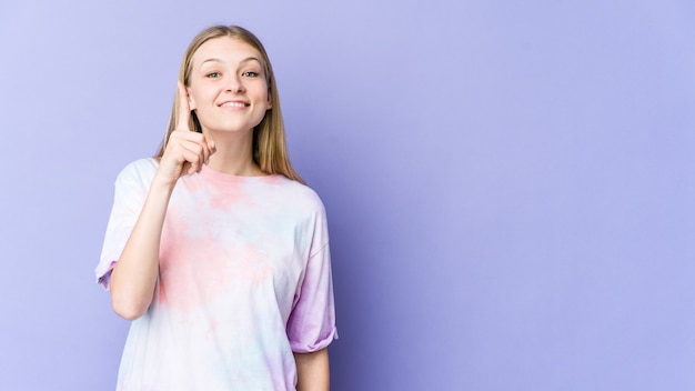 Mujer rubia joven aislada sobre fondo púrpura que muestra el número uno con el dedo.