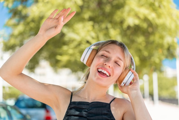 Mujer rubia joven al aire libre escuchando música y bailando