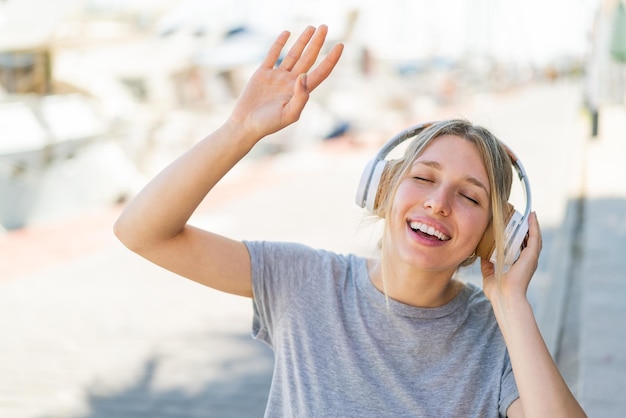 Mujer rubia joven al aire libre escuchando música y bailando