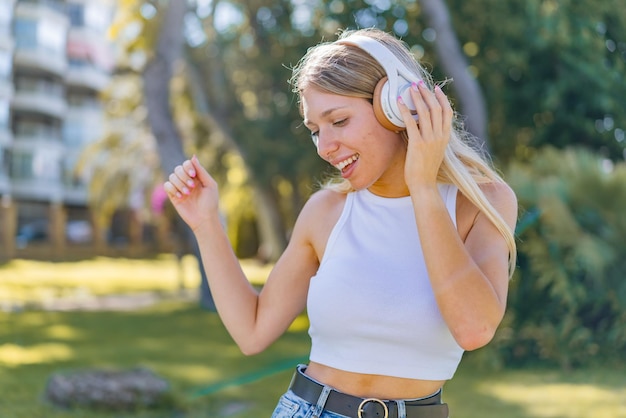 Mujer rubia joven al aire libre escuchando música y bailando